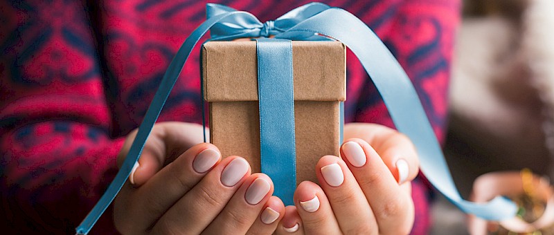 Ein Geschenk-Bild mit Händen und einem Geschenk mit blauer Schleife
